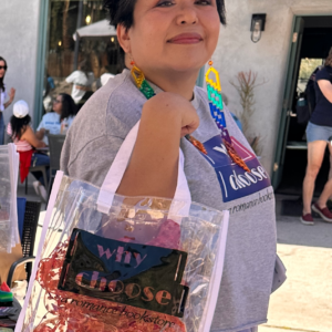 Photo of a woman with short hair holding a clear bag with ribbon inside it over her arm